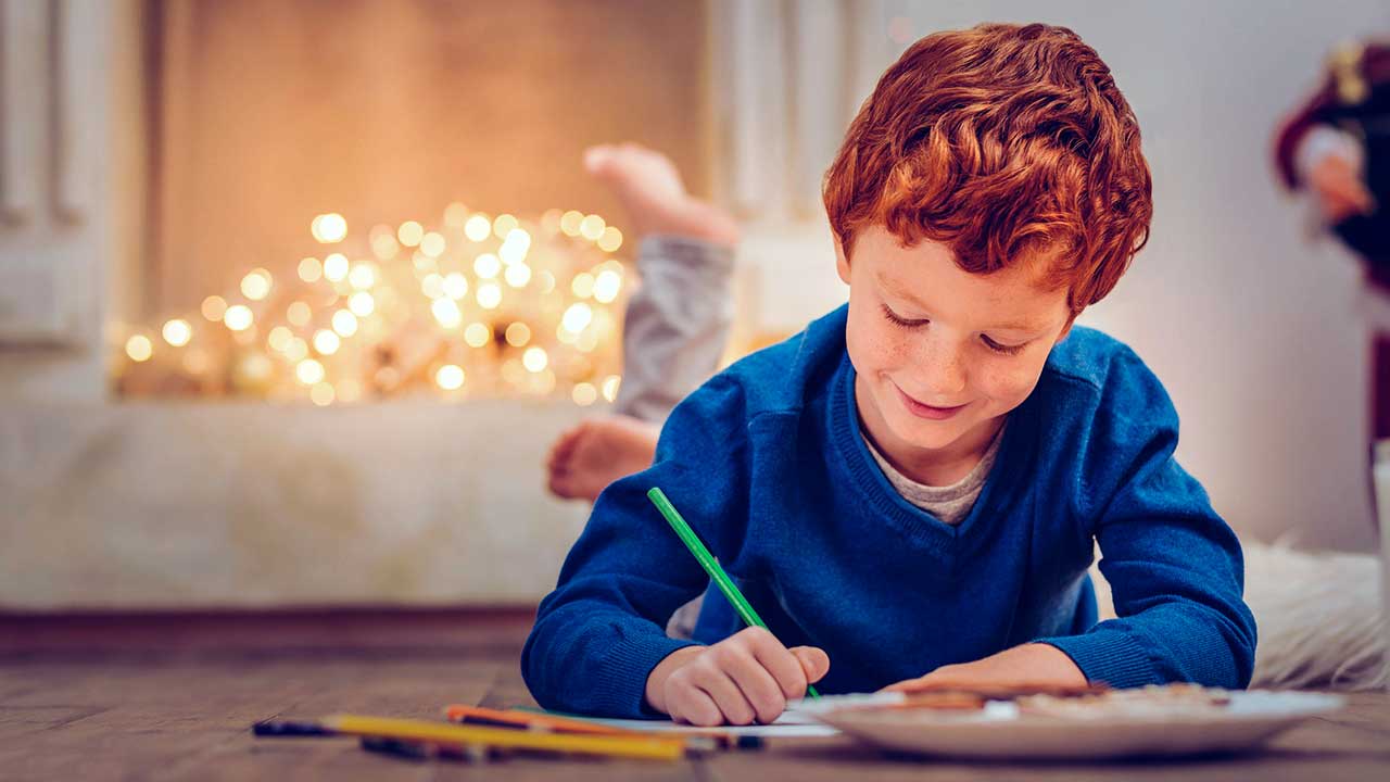 Junge liegt am Boden und schreibt einen Brief, im Hintergrund sind Lämpchen