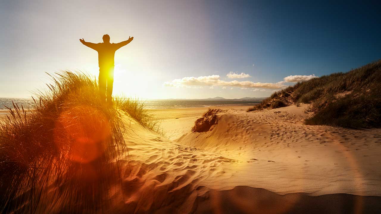 Mann steht auf Stranddüne und erhebt seine Hände