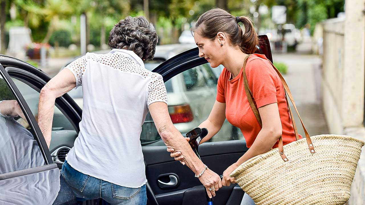 jüngerer Frau hilft älterer Frau ins Auto